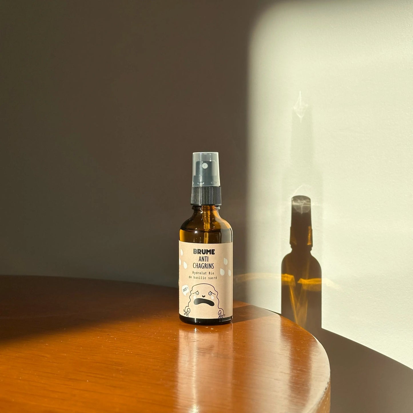 Image d'un Flacon de Brume Anti-Chagrins à l'Hydrolat Bio de Basilic Sacré pour Enfants, mis en scène sur une table en bois, éclairé par une lumière dorée de fin de journée.