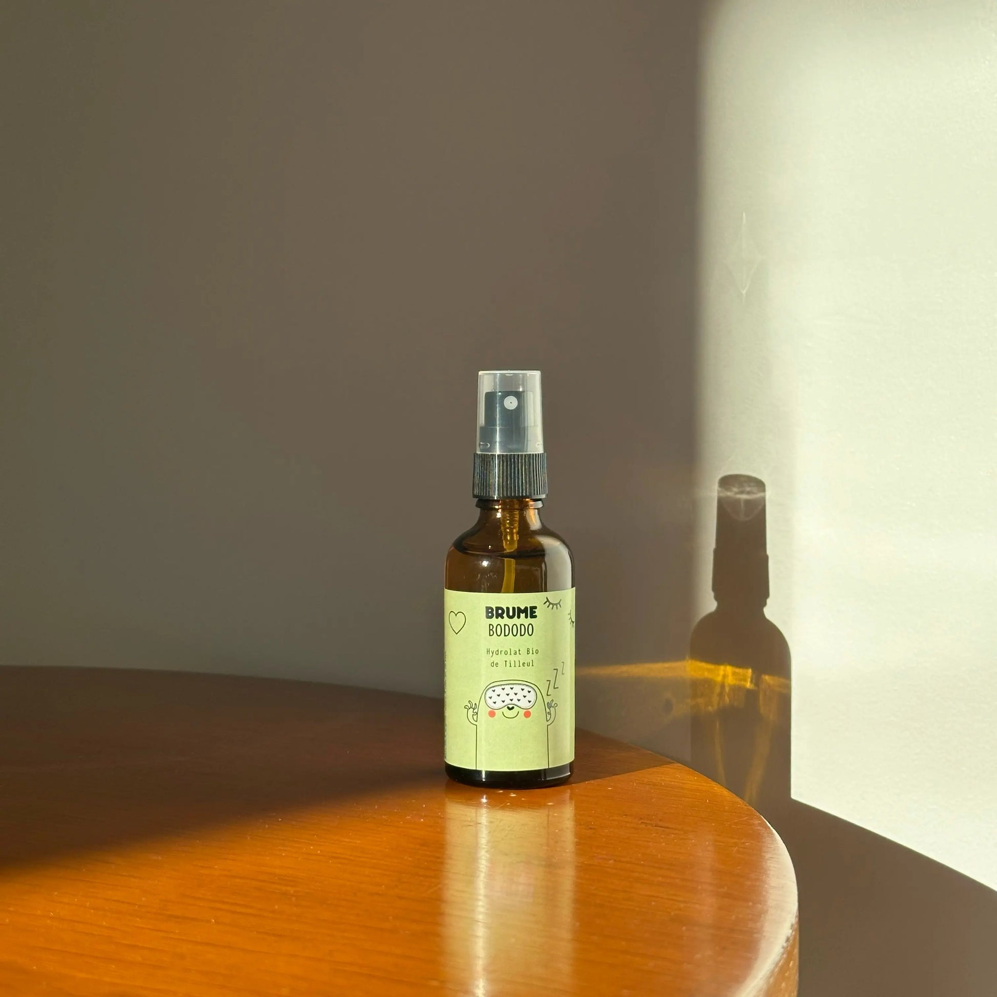 Image d'un Flacon de Brume Bododo à l'Hydrolat Bio de Tilleul pour Enfants, mis en scène sur une table en bois, éclairé par une lumière dorée de fin de journée.
